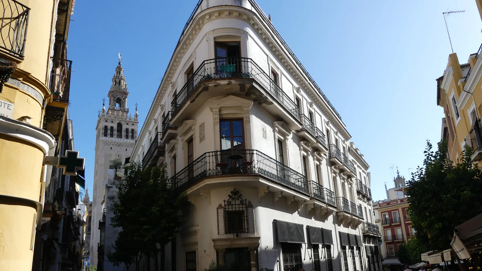 Roh ulice v centru Sevilly s nárožní budovou s balkony a věží Giralda tyčící se v pozadí pod modrým nebem