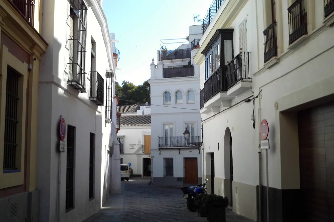 Úzká bíle omítnutá ulička Calle Dean Miranda s kovanými balkony a prosklenou galerií