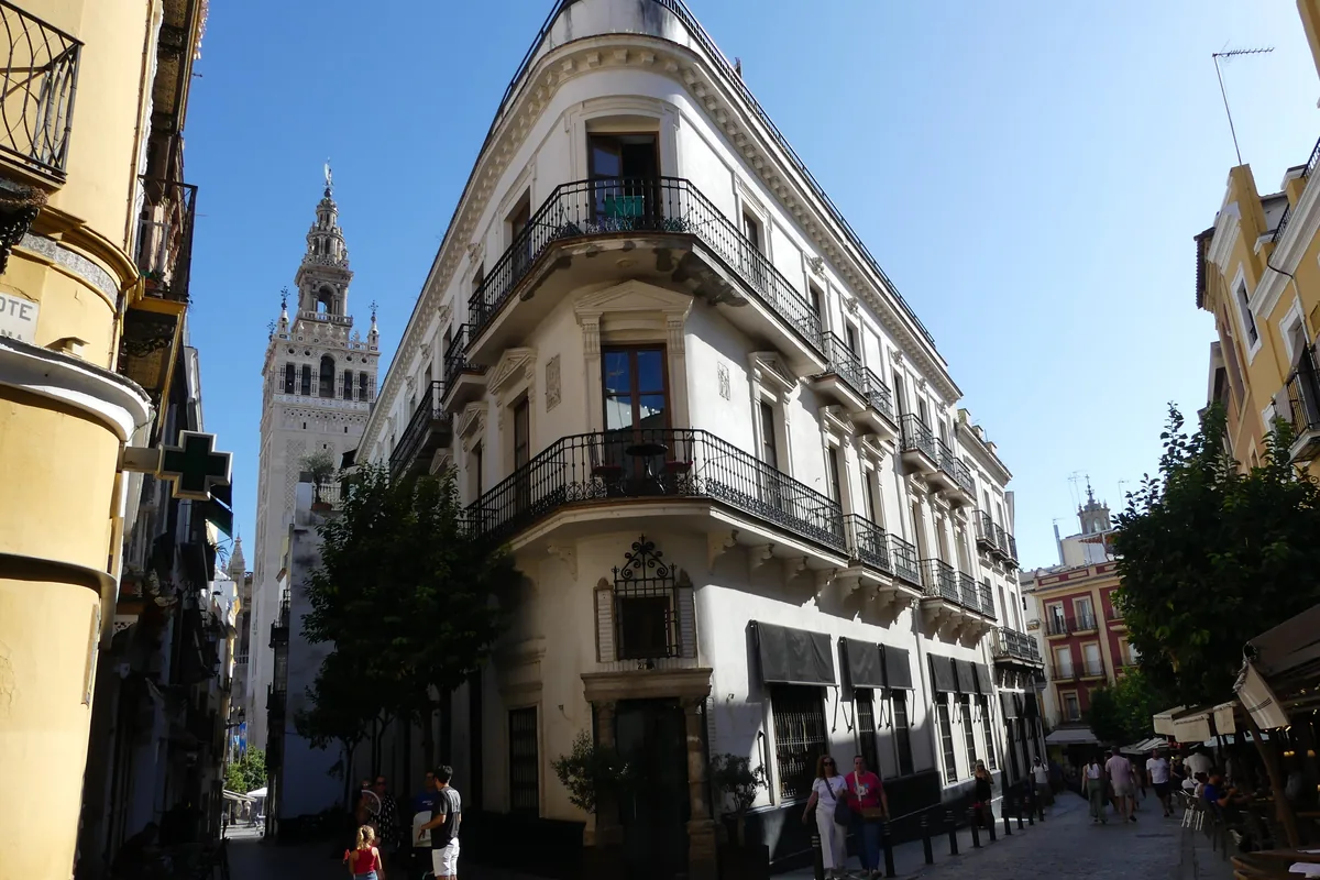 Roh ulice v centru Sevilly s nárožní budovou s balkony a věží Giralda tyčící se v pozadí